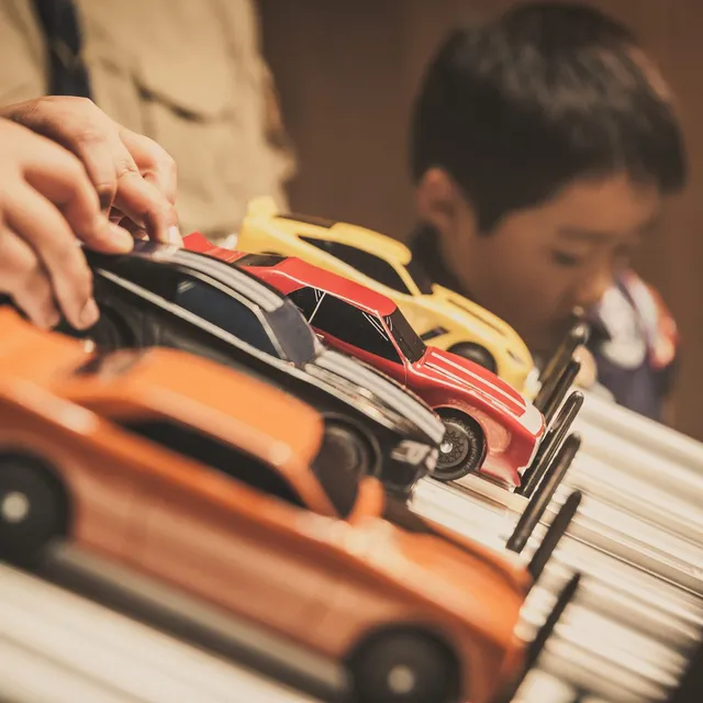 Pinewood Derby cars lined up at the starting gate as a Scout looks on